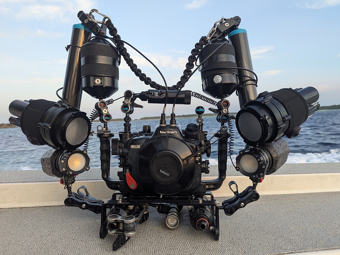 a_camera_in_underwater_housing_with_lots_of_attachments_sits_in_front_of_water.jpeg